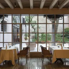 Tavoli apparecchiati in un elegante ristorante stellato Veneto, con vista su un cortile interno.