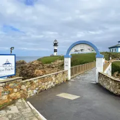 El faro de Ribadeo, con su icónico diseño blanco y negro, se alza sobre un acantilado verde. Un puente arqueado conduce a la isla.