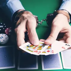 Kajdanki na rękach gracza, karty i żetony na zielonym stole symbolizują uzależnienie od hazardu i jego konsekwencje.