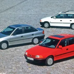 Trzy Ople Astra F: czerwony hatchback, srebrny sedan i białe kombi. Wśród nich wyróżnia się sportowy Opel Astra F GSI.