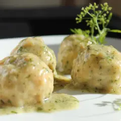 Quattro polpette in umido, ricoperte da una salsa cremosa alle erbe, servite su un piatto bianco con guarnizione di prezzemolo.
