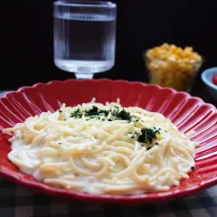 En krämig mac and cheese med persilja på en röd tallrik. Bredvid syns en sallad och ett glas vatten.