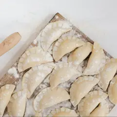Surowe pierogi ruskie ułożone na desce, obok wałek do ciasta.