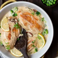 Delizioso pollo al vino bianco in salsa cremosa con broccoli, piselli e fette di limone, guarnito con prezzemolo fresco.