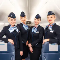 Uśmiechnięte stewardessy Enter Air w granatowych mundurkach i chustach z logo linii. Czy Enter Air jest bezpieczny? Tak, z taką załogą podróż będzie komfortowa.
