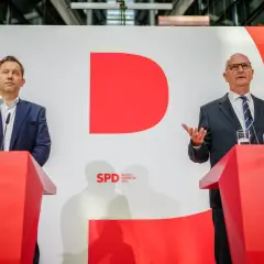 Zwei Männer stehen an roten Rednerpulten vor einer großen roten "D"-Grafik. Sie sprechen über das wahlergebnis brandenburg.