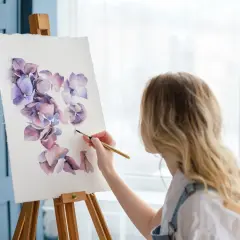 Kobieta maluje akwarelami fioletowe kwiaty. To inspiracja, jak być kreatywnym, tworząc piękno.