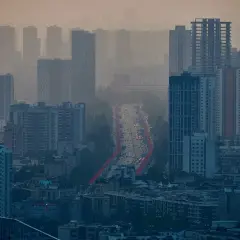 Gęsta zabudowa miejska w smogu. Widok na ruchliwą drogę z samochodami. Jak zapobiegać smogowi? Zmniejszyć emisję spalin.