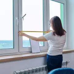 Une femme mesure une fenêtre, pensant à l'avantage d'un achat immobilier neuf pour personnaliser son espace.