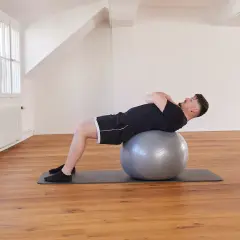 Un homme effectue un exercice avec ballon, le dos courbé sur le ballon de gym, les mains croisées sur la poitrine.