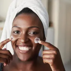Sonrisa radiante de mujer con toalla en la cabeza, aplicándose crema. Un vistazo al **retinol antes y después** para una piel luminosa.