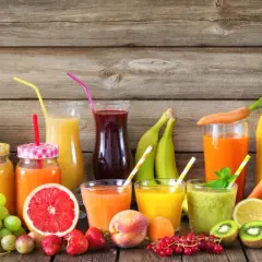 Varietà di bevande colorate e freschi estratti di frutta, con frutta intera e a fette su uno sfondo di legno.