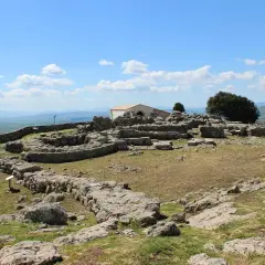 Rovine del santuario nuragico di Santa Vittoria sotto un cielo azzurro con nuvole bianche.