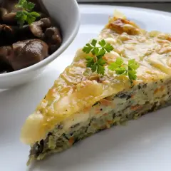 Kawałek zapiekanki z cukinii z warzywami i serem, podany z duszonymi grzybami.