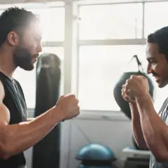Two men spar in a gym, channeling the intensity of a Rocky Marciano workout. Punching bags and bright windows frame their focused faces.