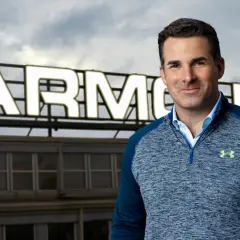 Mężczyzna w bluzie Under Armour na tle budynku z napisem ARMOUR.