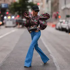 Modna kobieta w jeansach dzwonach i kwiecistej bluzce z bufiastymi rękawami, prezentująca stylowe jeansy dzwony stylizacje na ulicy.