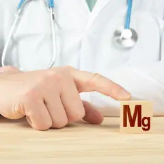 Lekarz w białym kitlu wskazuje palcem na kostkę z napisem "Mg".