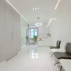 Nowoczesna poczekalnia kliniki estetycznej z białym marmurem, lustrami i wygodnymi fotelami.
