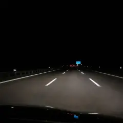 Fahrt über die Autobahn nachts. Scheinwerfer beleuchten die Fahrbahn, weiße Linien weisen den Weg in die Dunkelheit.