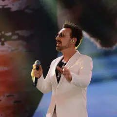 Mateusz Ziółko w białej marynarce śpiewa do mikrofonu na scenie.