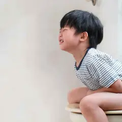 Niño de 5 a 10 años con estreñimiento, sentado en el inodoro con dolor y esfuerzo.