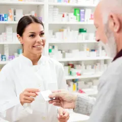 Farmaceutka podaje starszemu panu opakowanie leku, sugerując eliquis zamiennik.