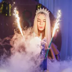 Dziewczyna w koronie zdmuchuje świeczki na torcie z fajerwerkami.