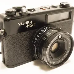 A black Yashica MG-1 camera with a leather strap. The lens reads "YASHINON 45mm 1:2.8".