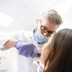 Dentysta w masce i rękawiczkach wykonuje borowanie zęba pacjentowi.