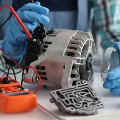 Mechanik w niebieskich rękawiczkach sprawdza alternator multimetrem. Objawy awarii alternatora mogą być różne, ale diagnostyka jest kluczowa.