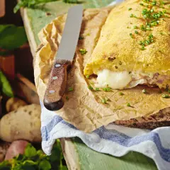 Herzhaft gefüllte polpette di patate, goldbraun paniert, mit geschmolzenem Käse im Inneren. Frische Kartoffeln liegen daneben.