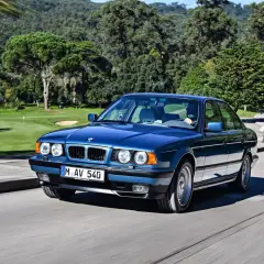 Niebieskie BMW E34 z lat 90. sunie po krętej drodze, mijając malownicze pole golfowe.