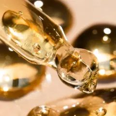 Kropla złotego serum z pipety, zawierającego sodium myreth sulfate, lśni na tle rozmytych, błyszczących kulek.