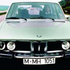 Klasyczne bmw e3 pędzi autostradą. Kierowca w garniturze pewnie trzyma kierownicę.