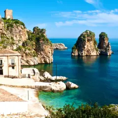 Torri e case antiche su scogliere rocciose, con faraglioni nel mare blu. Un paesaggio che evoca la storia dei bizantini in Sicilia.