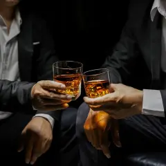 Deux hommes en costume portent des verres de whisky ambré, évoquant la définition d'un single malt : pur, authentique, une expérience unique.