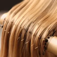 Delikatne rozczesywanie blond pasm przedłużanych włosów okrągłą szczotką. Poznaj sekrety, jak dbać o przedłużane włosy, by były lśniące i zdrowe.