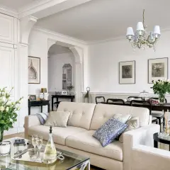 Eleganckie wnętrza w stylu hampton: jasna kanapa, szklany stolik z szampanem, bukiet róż i stylowe meble tworzą przytulną atmosferę.