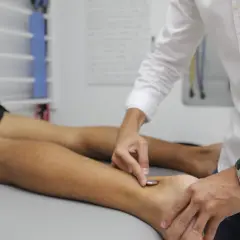 Fizjoterapeuta wykonuje zabieg na stopie pacjenta, co jest częścią rehabilitacji w ramach prewencji rentowej ZUS.