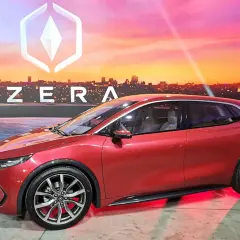 Czerwony samochód Izera na tle miejskiego krajobrazu o zachodzie słońca.