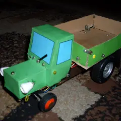 Zielony traktor z kartonu, z niebieskimi szybami i drewnianą skrzynią. Oto jak zrobić taki traktor z kartonu!