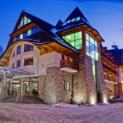 Elegancki hotel Crocus w zimowej scenerii, z kamienną fasadą i drewnianymi elementami, oświetlony nocą.