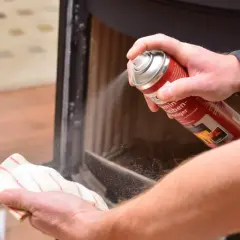 Hände reinigen den Kamin: Mit einem Reiniger wird der Ruß vom Schamottstein und Glas entfernt.