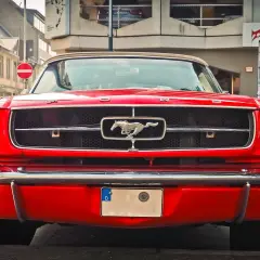 Czerwony Ford Mustang z lat 60. z emblematem galopującego konia na grillu.