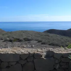 Vista desde una mesa roldan, con el mar azul al fondo y colinas áridas cubiertas de vegetación baja.
