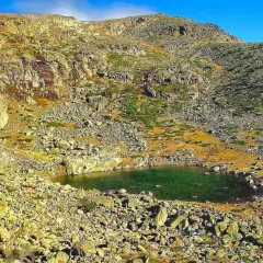 Laguna en la ruta de Peñalara, rodeada de rocas y vegetación de montaña bajo un cielo azul.