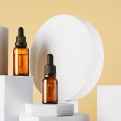 Dwie buteleczki z bursztynowego szkła z pipetkami, stojące na białych sześcianach. Pytanie, czy serum do twarzy się zmywa, pozostaje otwarte.