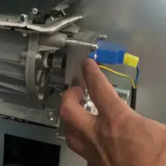 Main d'un homme manipulant le mécanisme d'un poêle à granulés, pour nettoyer le pressostat.