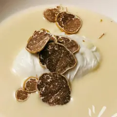 Uovo pochè su una cremosa fonduta, guarnito con scaglie di tartufo nero. Un piatto raffinato e profumato.